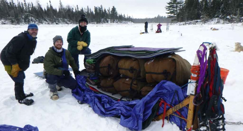 a group of gap year students pack a dog sled on a frozen snowy lake